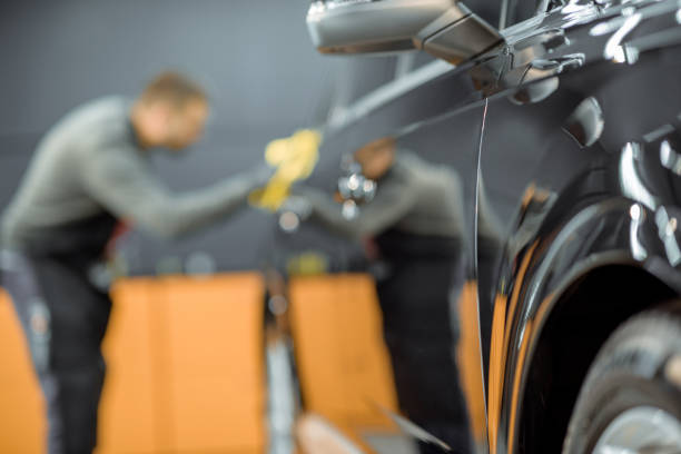 Car service worker wiping vehicle body with microfiber, examining glossy coating after the polishing procedure. Man blurred on the background